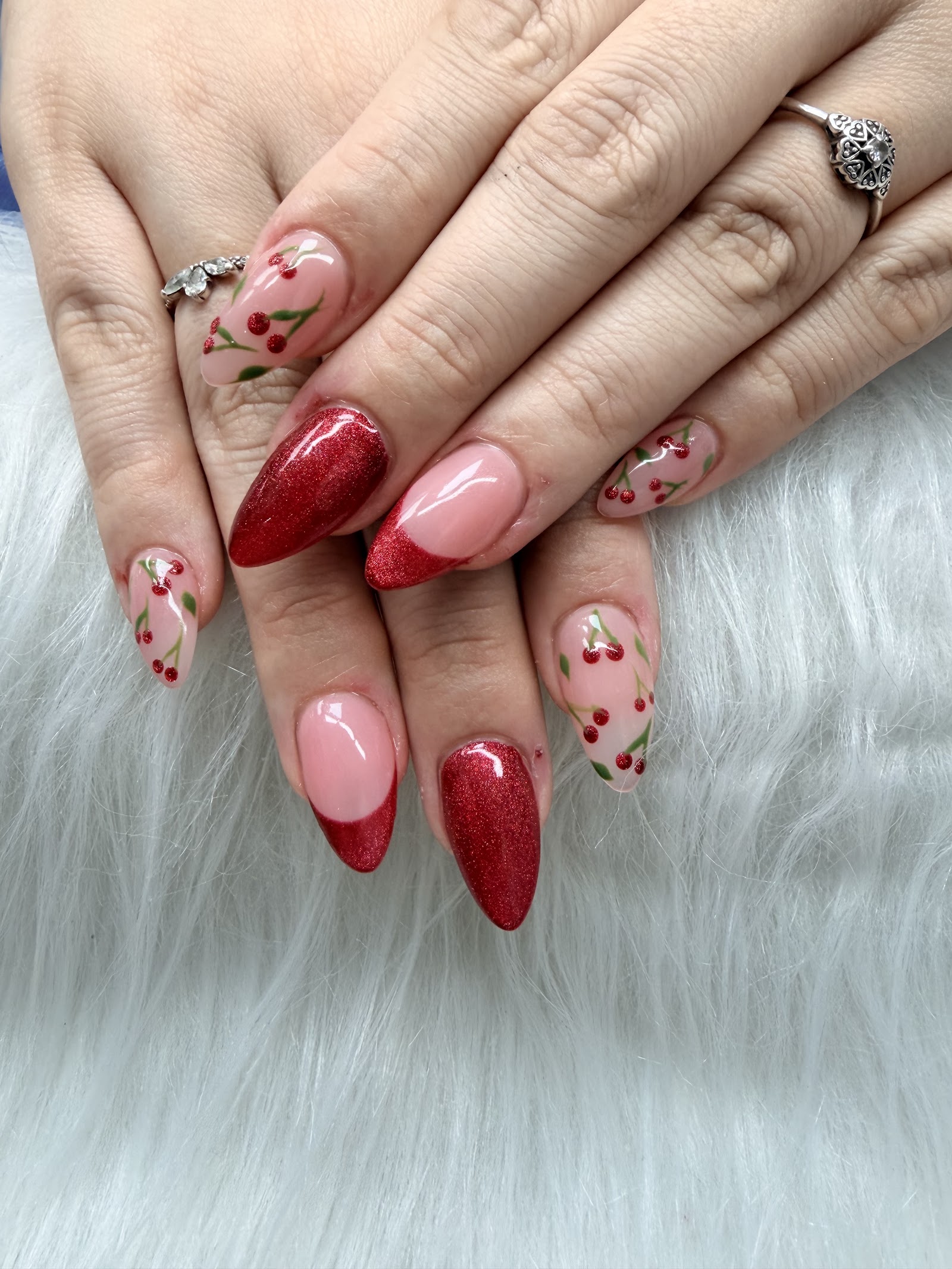 Almond nails mixing sparkling red glitter with clear nails hand-painted with little red cherries.