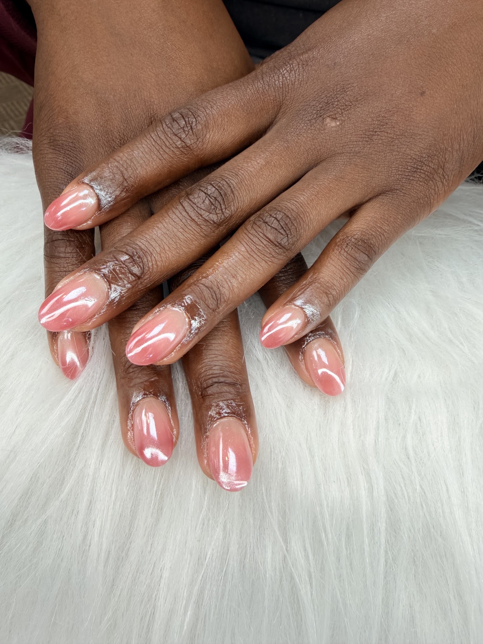 Short almond nails in a glazed pearl-pink chrome finish, resting on white fur.