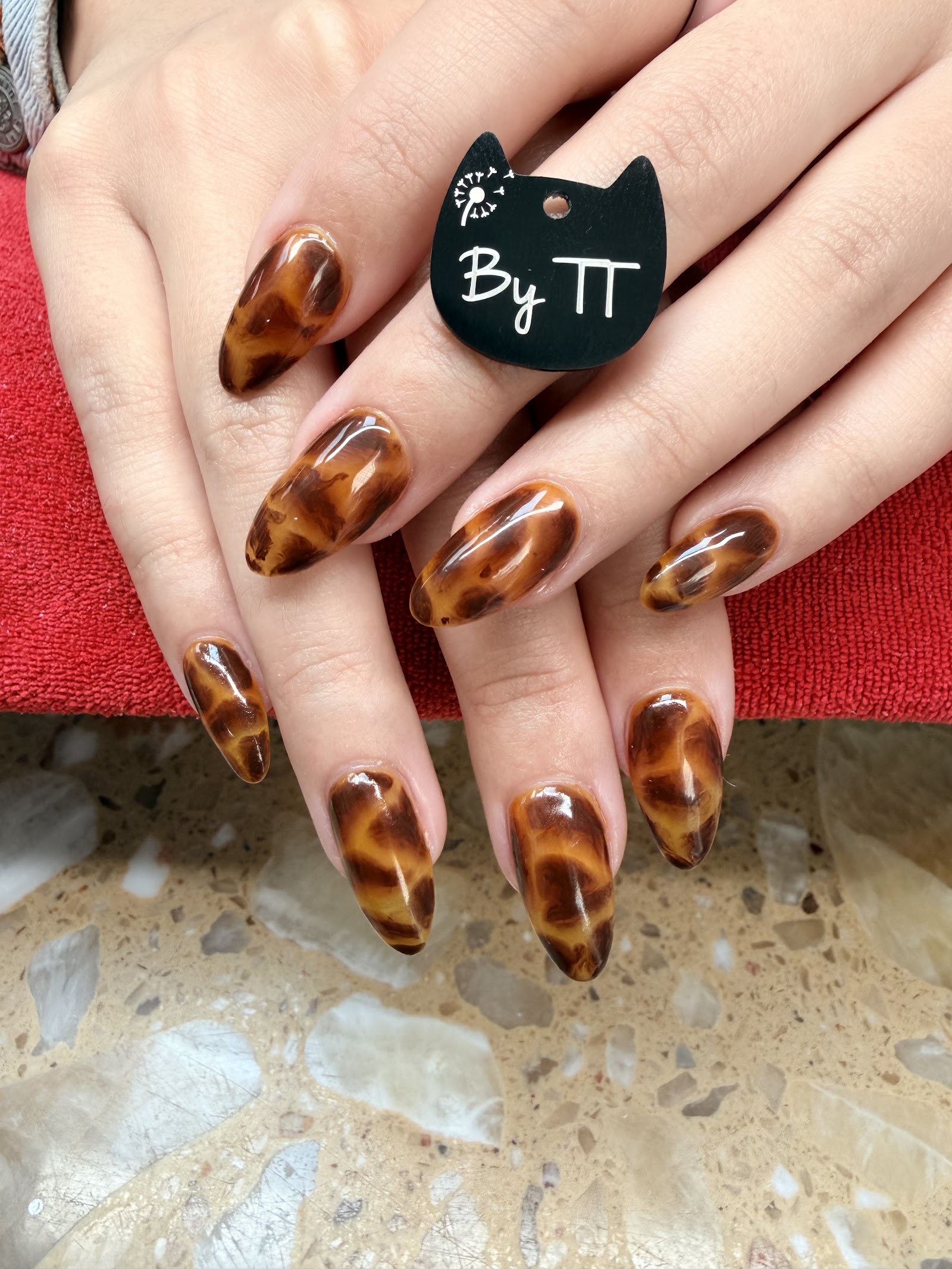 Long almond nails hand-painted in a glossy amber-and-brown tortoiseshell pattern.